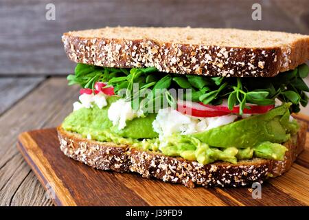 Superfood-Sandwich mit Vollkornbrot, Avocado, Eiweiß, Radieschen und Erbsen schießt auf Holzplatte Stockfoto