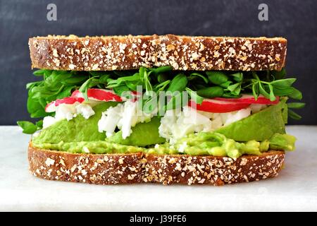 Superfood-Sandwich mit Vollkornbrot, Avocado, Eiweiß, Radieschen und Erbsen schießt auf Marmor vor schwarzem Hintergrund Stockfoto