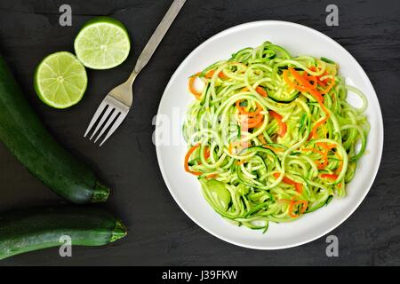 Gesunde Zucchini Nudel-Gericht mit Karotten und Kalk auf dunklem Schiefer, Draufsicht Stockfoto