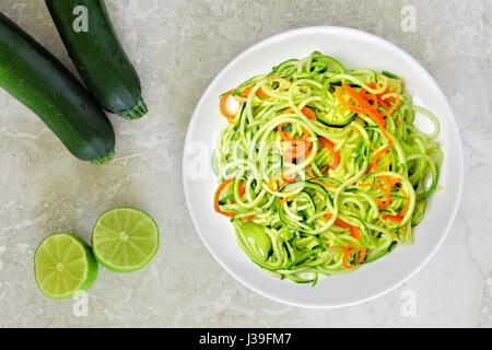Gesunde Zucchini Nudel-Gericht mit Karotten und Kalk auf weißem Marmor Hintergrund, Draufsicht Stockfoto