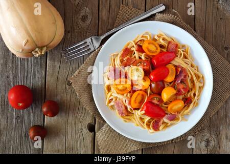 Cremige Kürbis Pasta mit Speck und Cherry-Tomaten, oben Blick auf rustikalen Holz Stockfoto