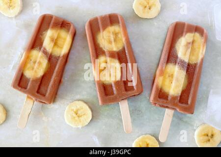 Schoko-Bananen Eis am Stiel mit in Scheiben geschnittenen Bananen auf weißem Marmor Hintergrund Stockfoto