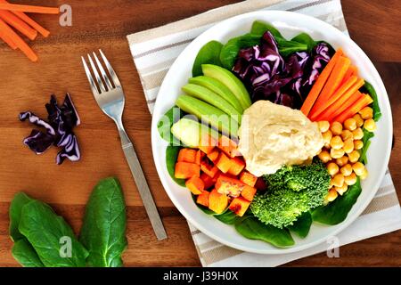 Gesundes Mittagessen Schüssel mit Avocado, Hummus und frisches Gemüse, obenliegende Szene auf Holztisch Stockfoto