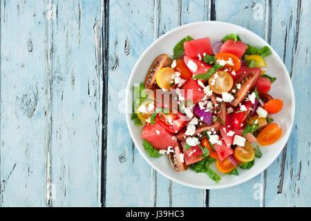 Wassermelone und gemischter Tomatensalat mit Feta-Käse, oben Blick auf rustikalen blau Holz Stockfoto