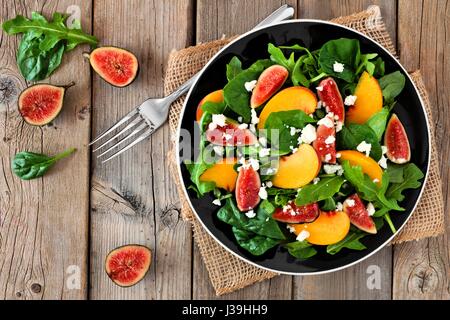 Herbst Salat aus Rucola, Spinat Feigen und Ziegenkäse in einer schwarzen Platte, Überkopf-Szene auf einem rustikalen hölzernen Hintergrund Stockfoto