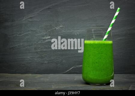 Grüne Grünkohl Smoothie in ein Glas mit Stroh auf einem dunklen Schiefer Stein Hintergrund Stockfoto