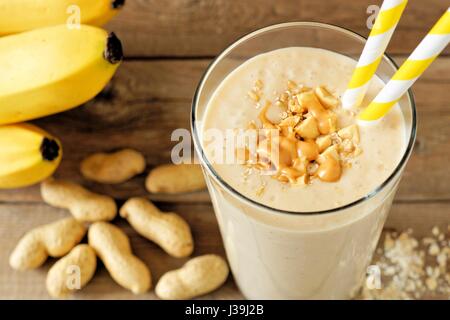 Erdnussbutter Banane Hafer Smoothie mit Papier Strohhalme auf rustikalen Tisch mit verstreuten Zutaten Stockfoto