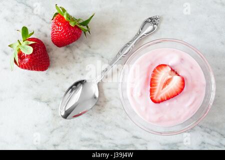 Aromatisierte Erdbeerjoghurt mit frischen Beeren, Draufsicht auf weißem Marmor Hintergrund Stockfoto