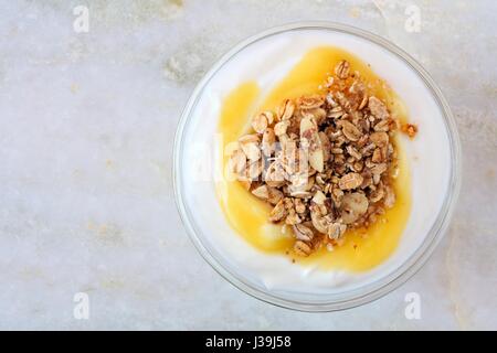 Zitrone aromatisierter Joghurt mit Müsli, Draufsicht auf weißem Marmor Hintergrund Stockfoto