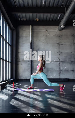 Seite Ansicht Portrait schöne junge Frau trägt weißes Tank-Top trainieren gegen graue Wand, Yoga oder Pilates Übung. Stehend in Krieger Stockfoto