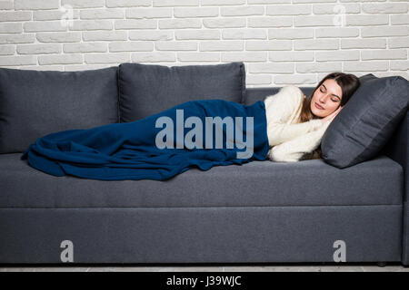 Junge Frau lag auf Sofa zu Hause schlafen bedeckt mit warmen Decke. Stockfoto