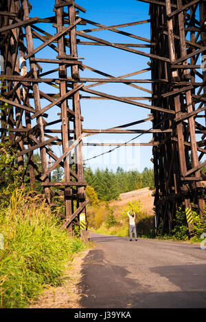 Hoher Strom 100 Jahre alte Eisenbahnbrücke über das Tal, durch das die Straße führt aus Baumstämmen als Stützen und Balken verbindet Stockfoto