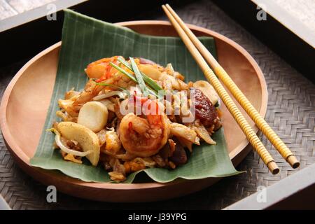 Char Kway Teow. Flache Reisnudeln mit Garnelen, Wurst, Sojabohnensprossen, Ei und Soja-Sauce gebraten. Auf einer hölzernen Platte ausgekleidet mit Bananenblatt serviert. Stockfoto