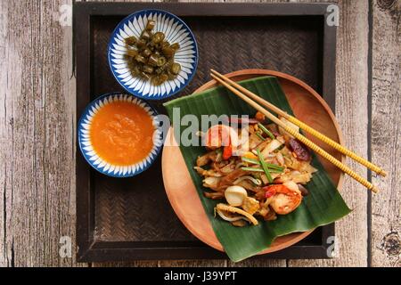 Char Kway Teow. Flache Reisnudeln mit Garnelen, Wurst, Sojabohnensprossen, Ei und Soja-Sauce gebraten. Auf einer hölzernen Platte ausgekleidet mit Bananenblatt serviert. Stockfoto