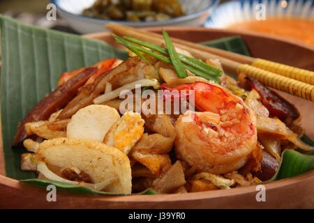 Char Kway Teow. Flache Reisnudeln mit Garnelen, Wurst, Sojabohnensprossen, Ei und Soja-Sauce gebraten. Auf einer hölzernen Platte ausgekleidet mit Bananenblatt serviert. Stockfoto