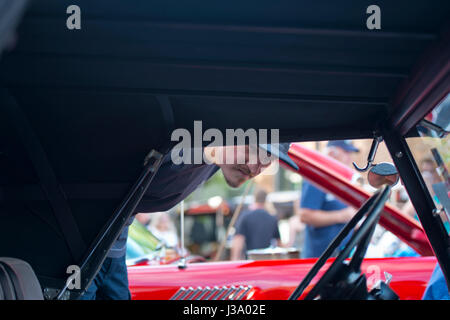 Ein Mann in einer Kappe schaut das Innere der restaurierten alten Rarität retro rotes Auto mit Klappdach auf die Ausstellung von Luxus Oldtimer auf der Anzeige Stockfoto