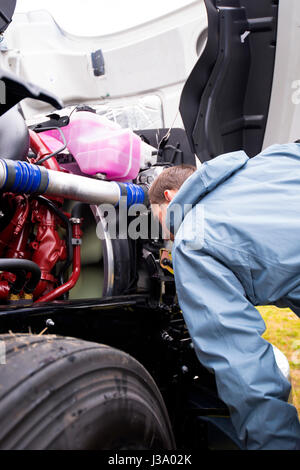 LKW-Fahrer von Sattelschlepper sorgfältig überprüfen Sie den laufenden Motor mit einem drehenden Lüfter auf dem modernen großen Rig Sattelschlepper, um die Haube zu öffnen Stockfoto