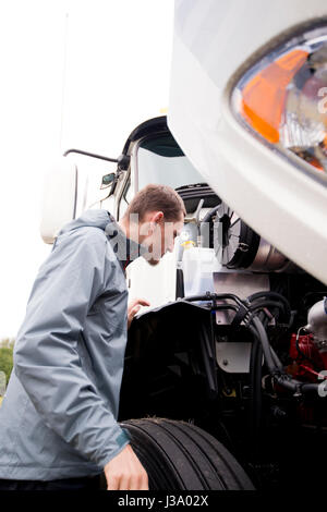 Professioneller LKW-Fahrer überprüft den Status seines Stahlpferdes mit einem Dieselmotor unter der offenen Haube eines riesigen modernen Sattelwagens Stockfoto
