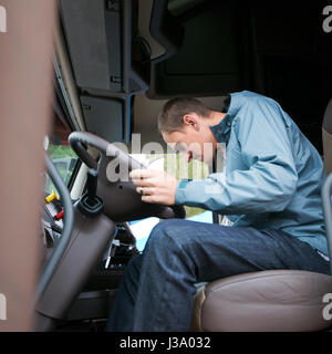 Young man Lkw-Fahrer sitzt in einer komfortablen Kabine des modernen Lkw und überprüfen Sie die Bereitschaft der Lkw-Elektronik-Systeme für den Einsatz auf der Autobahn Stockfoto