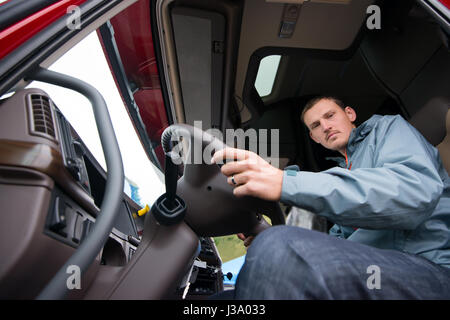 Ein junger LKW-Fahrer hinter dem Steuer der modernen komfortablen Kabine des großen Rig Semi-LKW mit einer hohen Kabine und öffnen Sie die Tür bereit, sich zu bewegen Stockfoto