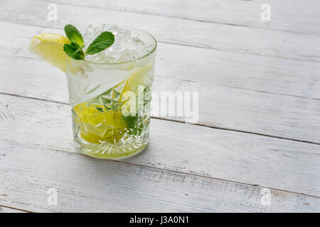 Cocktail mit Limetten, Eis und Pfefferminze auf weißem Hintergrund aus Holz. Stockfoto