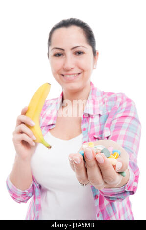 Lächelnde junge Frau, die mit Drogen in der einen Hand und einer Banane in der anderen auf weißem Hintergrund Stockfoto