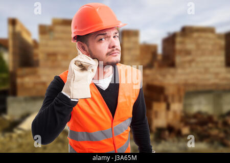 Neugierig Konstruktor in Schutzausrüstung hören einige flüstern oder die Nachrichten auf seinem Arbeitsplatz Stockfoto