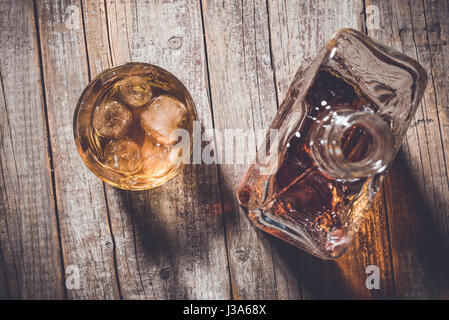 Overhead shot von Whiskey Flasche und Whiskey Glas mit Eiswürfeln auf einem alten Holztisch Stockfoto
