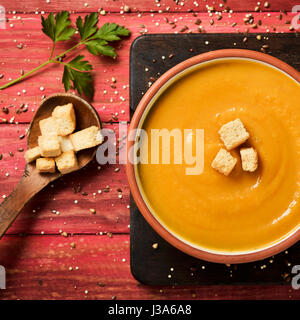 High-Angle Shot von einem Steingut-Schale mit Kürbispüree, garniert mit einigen Croutons auf einem roten rustikalen Holztisch Stockfoto