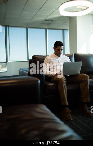 Ernst Kaufmann mit Laptop sitzend auf Sofa im beleuchteten Büro Stockfoto