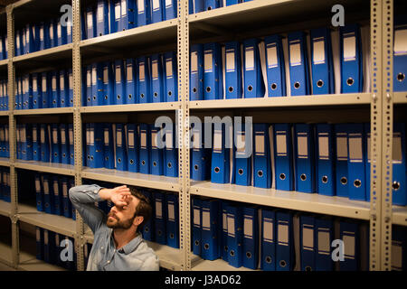Müde Geschäftsmann sitzen von Regalen in Datei Lagerraum Stockfoto