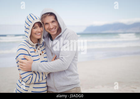 Porträt des Lächelns paar tragen Kapuzen Pullover am Strand im winter Stockfoto