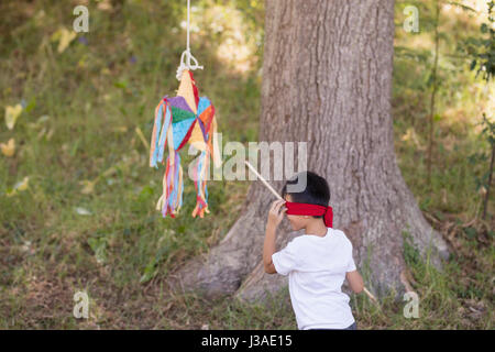 Mit verbundenen Augen junge schlagen Pinata vom Baum im Wald Stockfoto