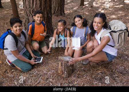 Hohen Winkel Porträt von Lehrer und Schüler kniend von Baumstumpf im Wald während der Exkursion Stockfoto