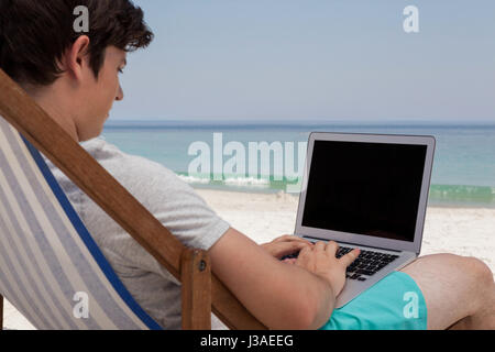 Mann mit Laptop sitzend auf Stuhl am Strand Stockfoto