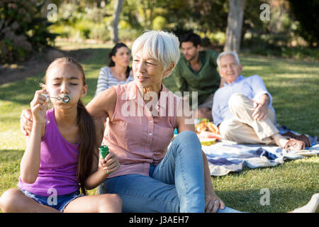 Großmutter ihre Enkelin bläst Seifenblasen im Park an einem sonnigen Tag zu betrachten Stockfoto