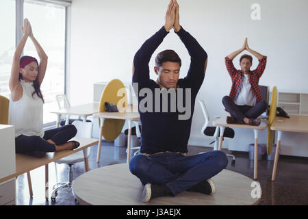 Geschäftskollegen Yoga beim Sitzen am Schreibtisch im Büro zu tun Stockfoto