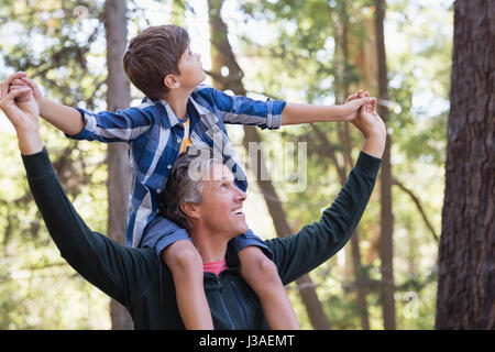 Glücklicher Vater mit Sohn auf Schultern beim Wandern im Wald Stockfoto