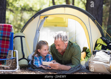 Vater und Tochter mit Mobiltelefon und entspannen Sie im Zelt am Campingplatz Stockfoto