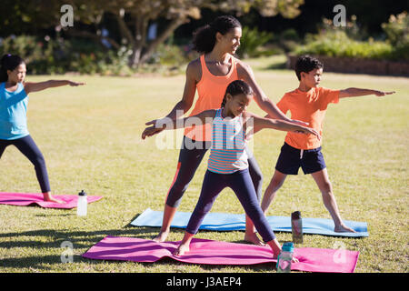 Junge weibliche Lehrer Prüfung Kinder Praciting Virabhadrasana II stellen im park Stockfoto