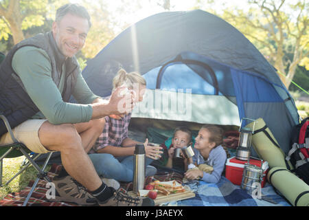 Familie lächelnd mit Snacks und Kaffee außerhalb des Zeltes auf Campingplatz Stockfoto