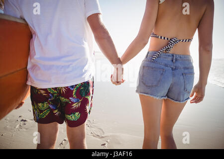 Mittelteil des Paares Hand in Hand am Strand im sonnigen Tag Stockfoto