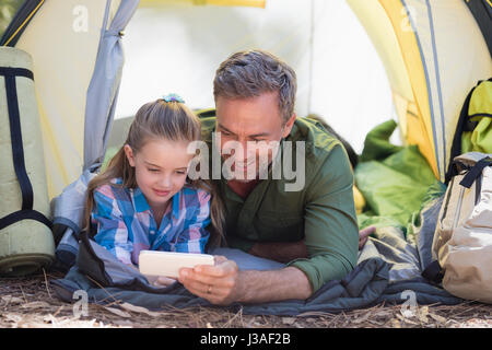 Vater und Tochter mit Handy bei einer Rast im Zelt am Campingplatz Stockfoto