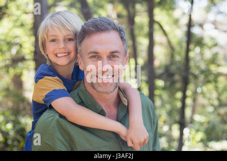 Porträt der lächelnden Vater Sohn im Wald Huckepack Stockfoto