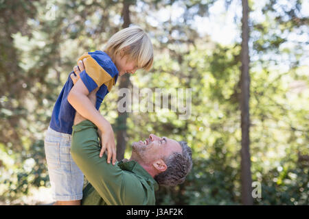 Seitenansicht des spielerischen Vater Sohn im Wald anheben Stockfoto