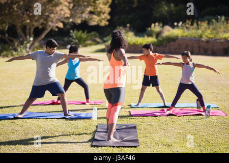 Weibliche Lehrer unterrichten Kinder Virabhadrasana II auf Matte im park Stockfoto