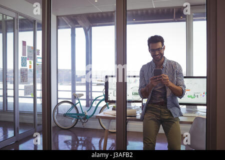 Lächelnde Geschäftsmann mit Handy beim Sitzen am Schreibtisch im Büro Stockfoto