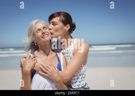 Junge Frau ihrer Mutter am Strand im sonnigen Tag küssen Stockfoto