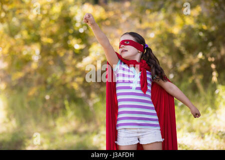 kleines Mädchen versucht zu fliegen, während des Tragens Superhelden-Kostüm auf Campingplatz Stockfoto