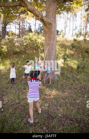 Rückansicht mit verbundenen Augen Mädchen schlagen Pinata hängen am Baum im Wald Stockfoto